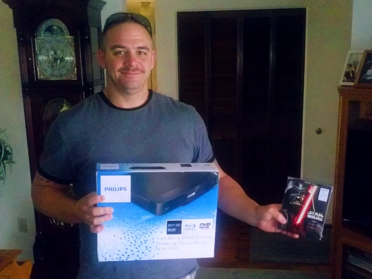 Billy Parsons smiling while holding his brand-new DVD player and Star Wars Trilogy DVD prize.